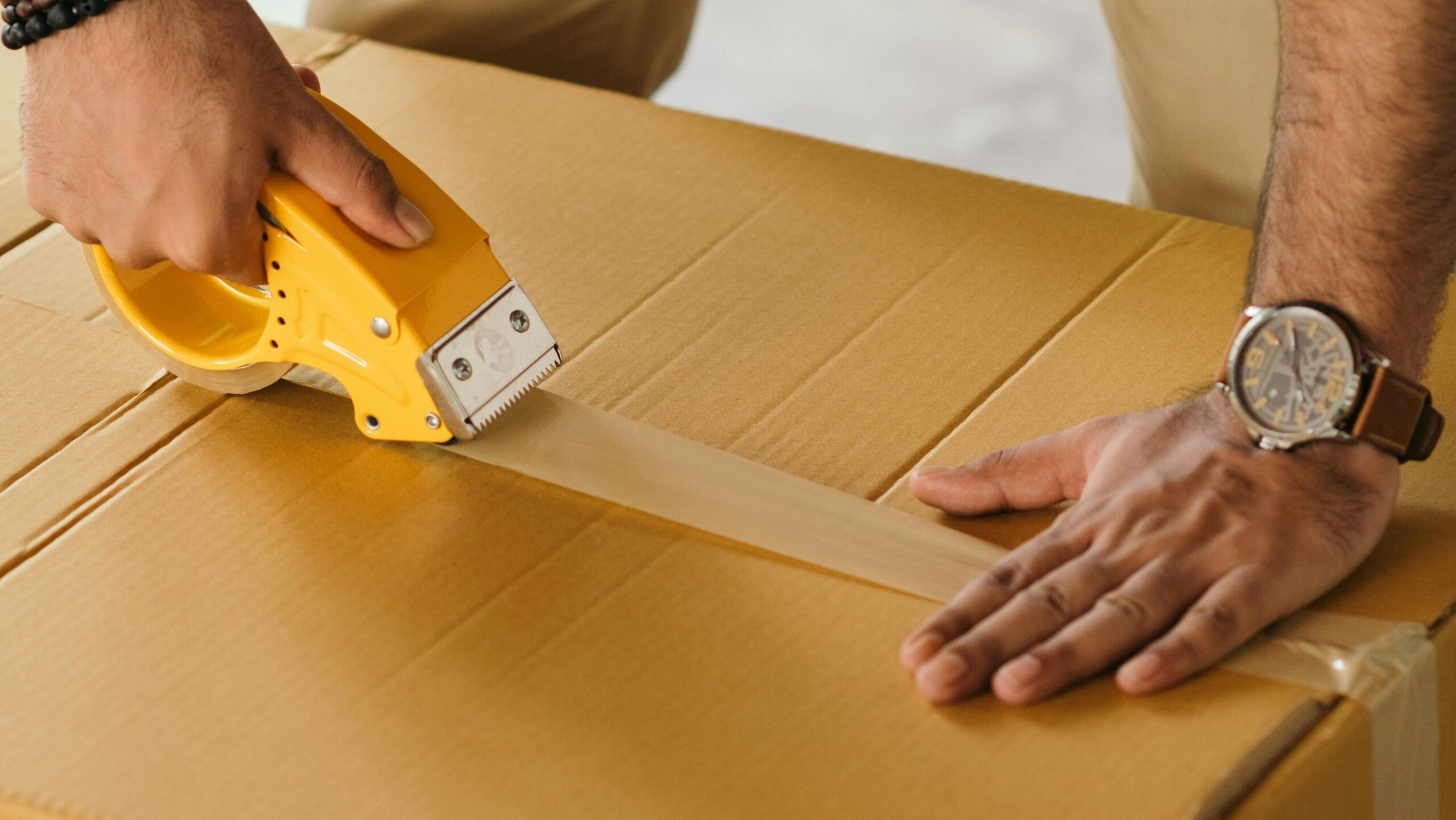 Unrecognizable man sealing box with duck tape while preparing for moving out